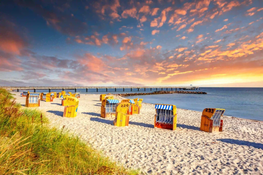 Perfekter Ostsee Urlaub mit Hund: Die besten Tipps und Tricks 2 Strandkörbe am Ostseestrand bei Sonnenuntergang mit farbenprächtigem Himmel und Seebrücke im Hintergrund – perfekt für einen Urlaub mit Hund an der Ostsee.