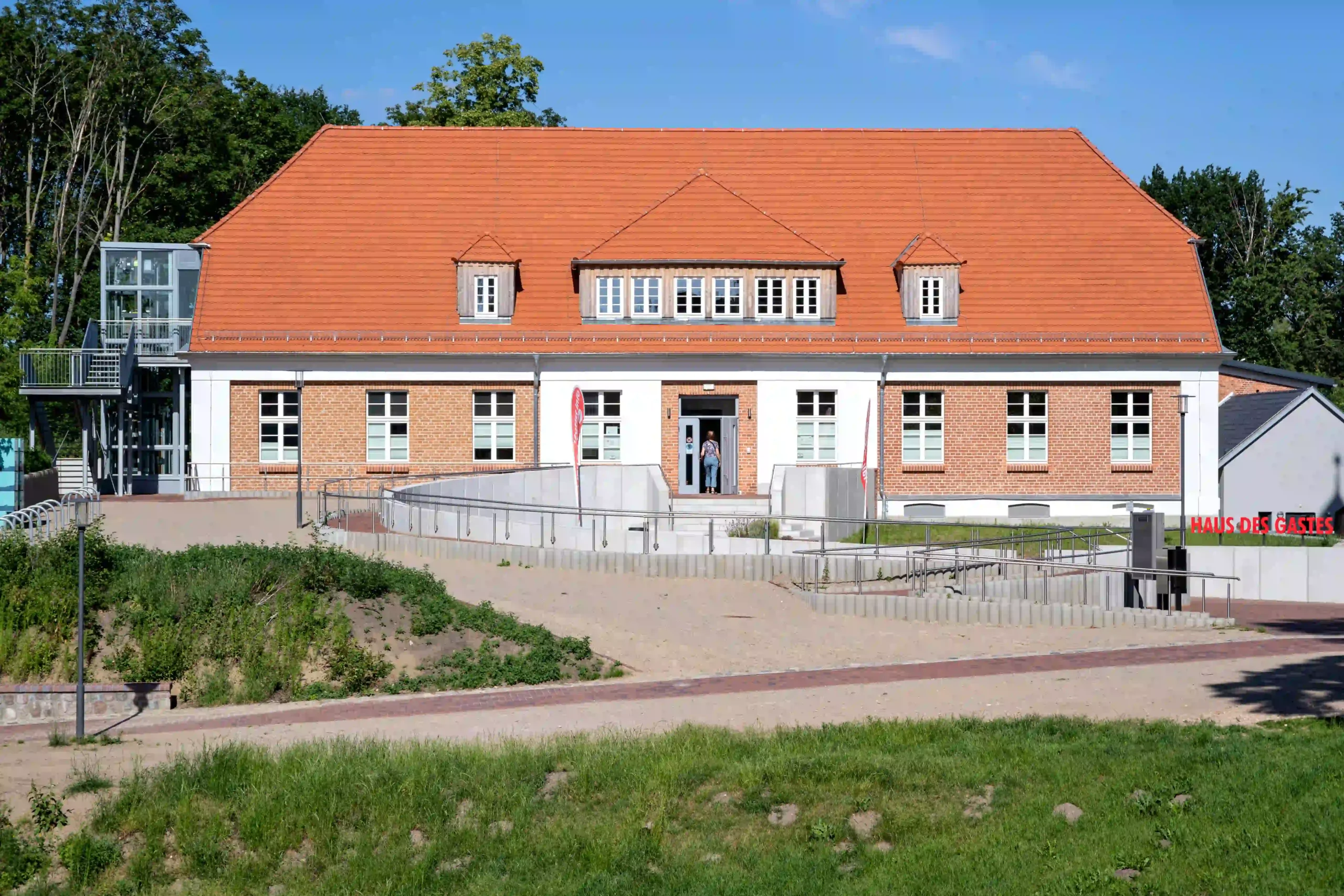Das Informationszentrum "Haus des Gastes" in Plau am See, ein modernes Gebäude mit weißer Fassade und rotem Ziegeldach, umgeben von Grünflächen.