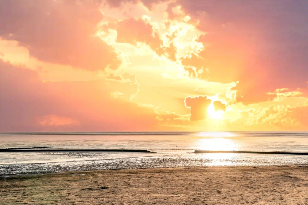 Norddeich mit Hund: Perfekter Nordsee-Urlaub mit Vierbeiner 1 Ein atemberaubender Sonnenuntergang über dem Wattenmeer in Norddeich mit dramatischen orangefarbenen Wolken und der spiegelnden Sonne auf dem Wasser. Ein magischer Moment, den man in Norddeich mit Hund erleben kann.