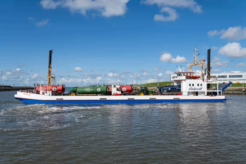 Norddeich mit Hund: Perfekter Nordsee-Urlaub mit Vierbeiner 7 Ein Transportschiff namens "FREJA SW" auf dem Wasser in Norddeich, beladen mit Landmaschinen, unter strahlend blauem Himmel mit Wolken. Ein interessanter Anblick am Hafen von Norddeich, auch wenn der Hund an der Leine bleiben sollte.