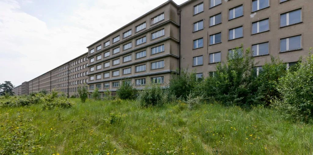 Urlaub mit Hund in Prora auf Rügen – Der perfekte Guide 7 Langer, mehrstöckiger Betonbau der Prora auf Rügen mit verwildertem Gras und bewölktem Himmel im Hintergrund