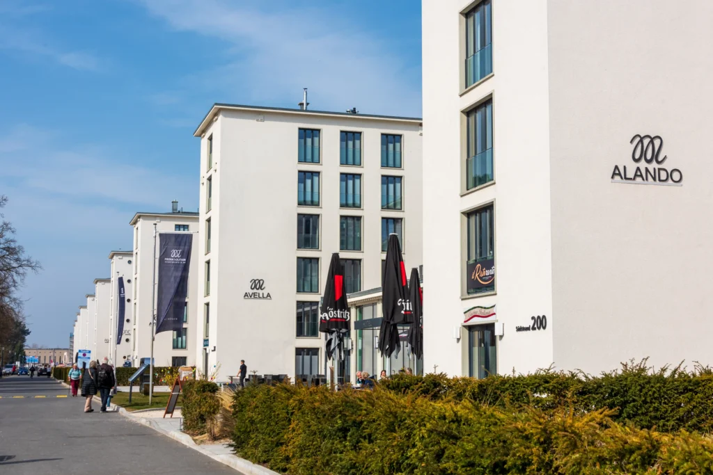 Urlaub mit Hund in Prora auf Rügen – Der perfekte Guide 4 Moderne weiße Gebäude mit Cafés und Balkonen an einer Straße in Prora auf Rügen bei klarem Himmel und Menschen.