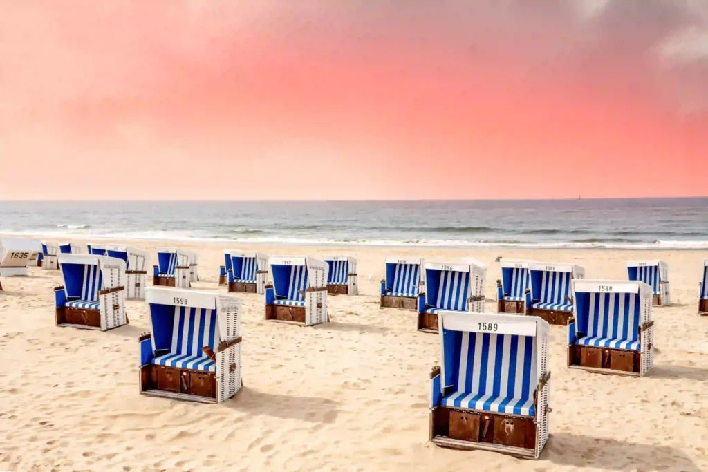 Sylt mit Hund: Dein ultimativer Guide für den perfekten Inselurlaub 11 Zahlreiche Strandkörbe mit blauen und weißen Streifen am weitläufigen Sandstrand von Sylt unter einem rötlichen Himmel – entspannte Tage auf Sylt mit Hund genießen.