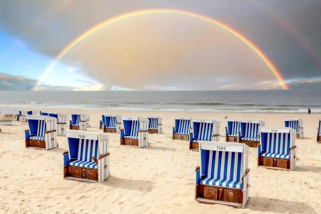 Sylt mit Hund: Dein ultimativer Guide für den perfekten Inselurlaub 3 Strandlandschaft auf Sylt mit zahlreichen gestreiften Strandkörben und einem beeindruckenden Regenbogen über dem Meer – unvergessliche Momente auf Sylt mit Hund erleben.