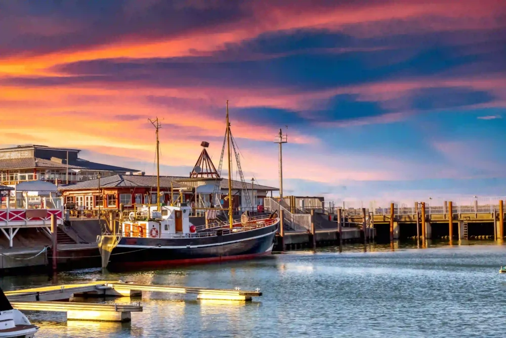 Sylt mit Hund: Dein ultimativer Guide für den perfekten Inselurlaub 8 Malerischer Hafen auf Sylt bei Sonnenuntergang mit einem traditionellen Segelboot und bunten Wolken am Himmel – perfekt für Spaziergänge mit Hund auf Sylt.
