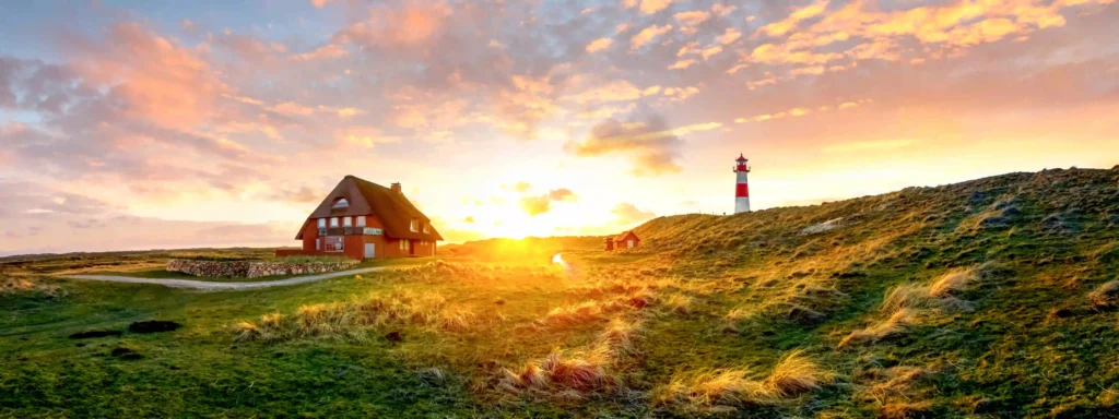 Sylt mit Hund: Dein ultimativer Guide für den perfekten Inselurlaub 1 Weitläufige Dünenlandschaft auf Sylt mit einem traditionellen Reetdachhaus und dem rot-weißen Leuchtturm bei Sonnenuntergang – ideal für lange Spaziergänge auf Sylt mit Hund.