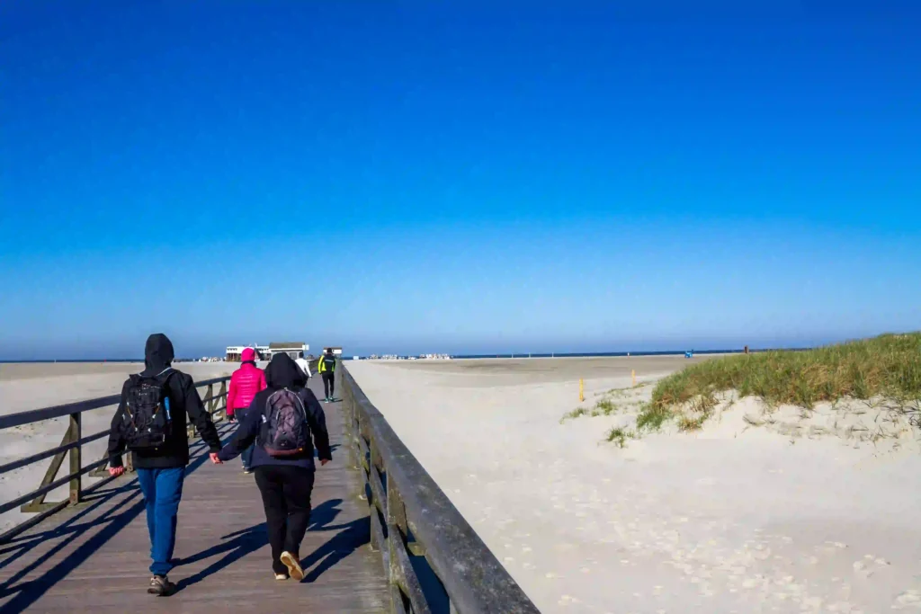 Urlaub mit Hund in St. Peter-Ording: Dein kompletter Guide für entspannte Ferien 8 Spaziergänger auf einem Holzsteg am breiten Sandstrand von St. Peter-Ording.