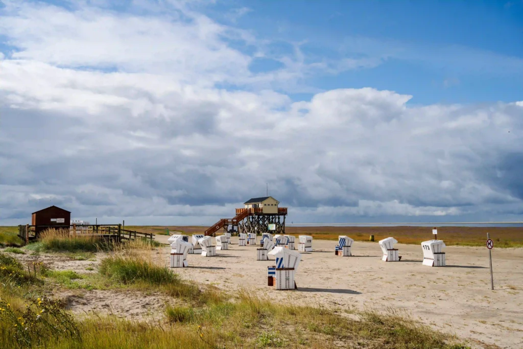 Urlaub mit Hund in St. Peter-Ording: Dein kompletter Guide für entspannte Ferien 4 Strandkörbe und Pfahlbauten am Sandstrand von St. Peter-Ording unter bewölktem Himmel.