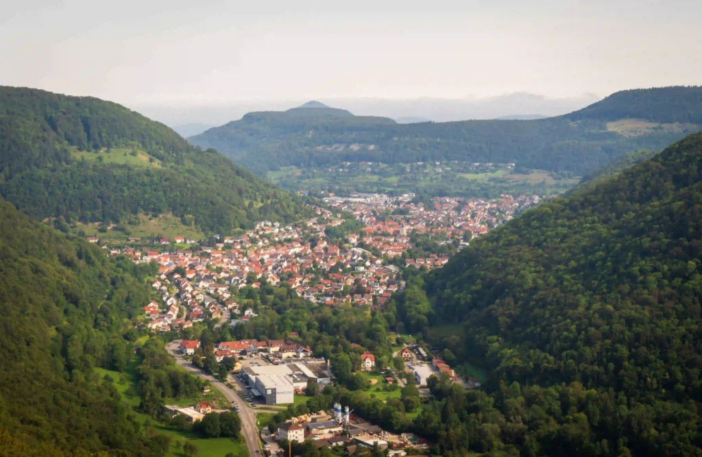 Wandern mit Hund am Schloss Lichtenstein erleben 1 Eine weite Ansicht eines Tals mit einer Stadt, umgeben von grünen Hügeln, im Hintergrund von Schloss Lichtenstein.