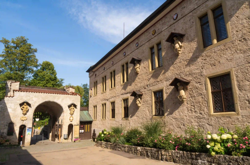 Wandern mit Hund am Schloss Lichtenstein erleben 2 Ein Gebäude am Fuße des Schloss Lichtenstein, mit einer steinernen Fassade, Torbögen und blühenden Blumenbeeten.