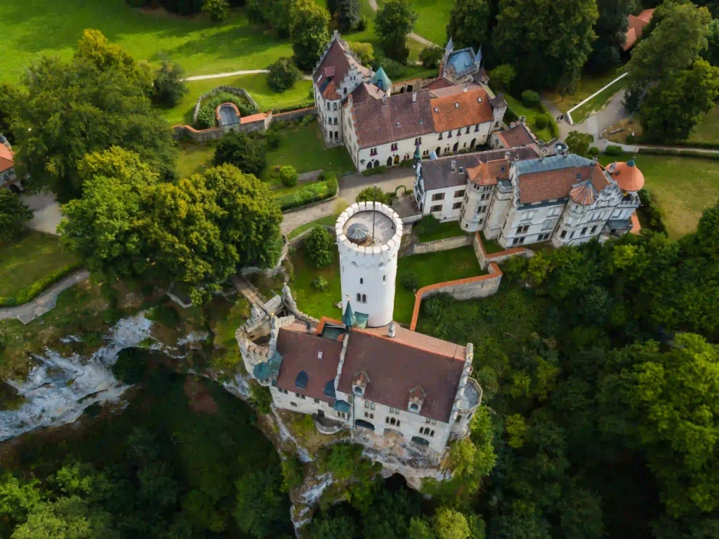 Wandern mit Hund am Schloss Lichtenstein erleben 5 Eine Vogelperspektive von Schloss Lichtenstein, die die gesamte Burganlage mit ihren verschiedenen Gebäuden, Höfen und den umliegenden Grünflächen zeigt.