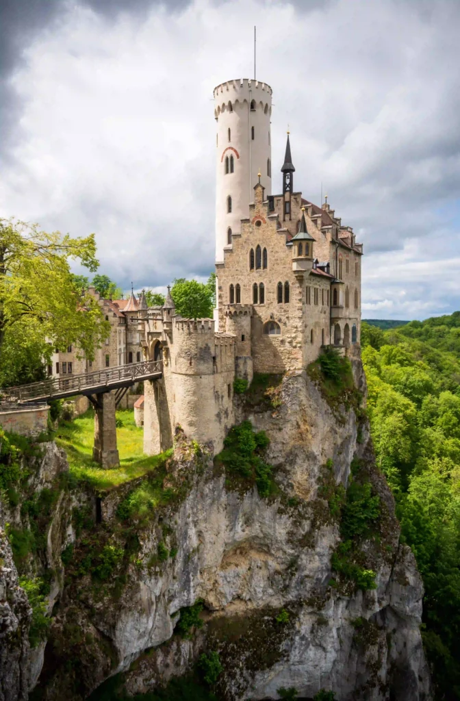 Wandern mit Hund am Schloss Lichtenstein erleben 6 Schloss Lichtenstein, eine historische Burg auf einer felsigen Klippe, umgeben von dichtem Grün und einem dramatischen Himmel.