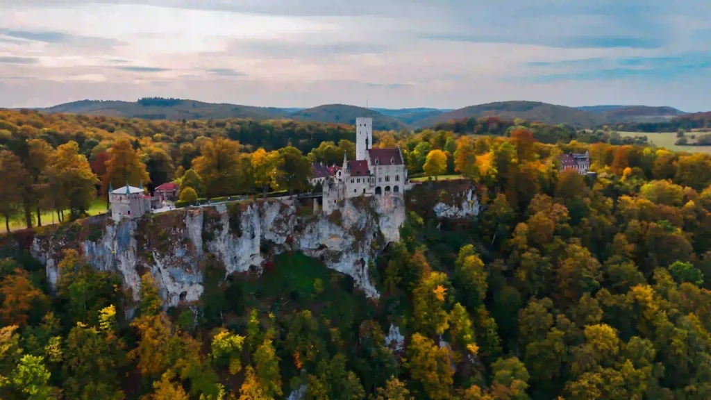 Wandern mit Hund am Schloss Lichtenstein erleben 8 Eine Luftaufnahme von Schloss Lichtenstein in der Herbstlandschaft, umgeben von Bäumen mit bunten Blättern und einer weiten Landschaft.