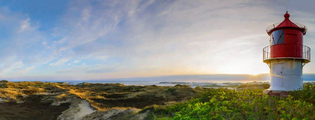 Amrum mit Hund: Perfekter Inselurlaub für Vierbeiner 1 Ikonischer Amrum Leuchtturm vor einem weiten Himmel und malerischer Dünenlandschaft bei Sonnenaufgang, ein Highlight für jeden Besuch in Amrum mit Hund.