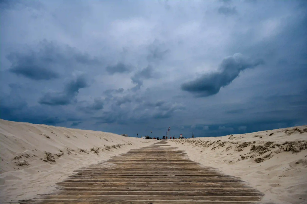 Amrum mit Hund: Perfekter Inselurlaub für Vierbeiner 6 Holzsteg führt über weitläufigen Sandstrand unter dramatischem Himmel, ideal für einen Spaziergang in Amrum mit Hund.