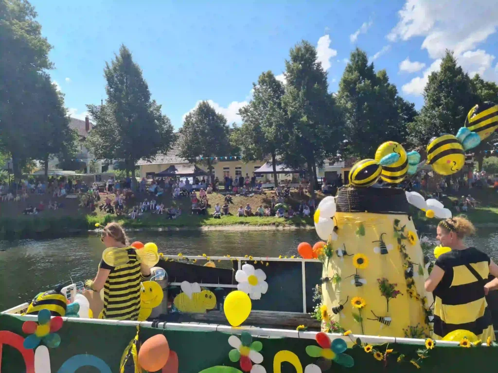 Badewannenrally Plau am See 2025 – Spaß und Action am Wasser 9 Detailansicht eines fantasievoll als Biene dekorierten Boots mit Teilnehmern in Bienenkostümen während der Badewannenrally in Plau am See. Am Ufer sitzen Zuschauer.