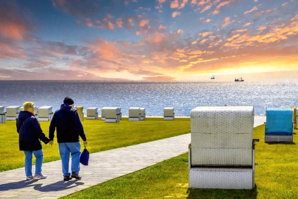 Büsum mit Hund: Perfekter Nordsee-Urlaub mit Vierbeiner 2 Paar macht einen Spaziergang entlang des Deichs bei Sonnenuntergang in Büsum, mit Strandkörben und der Nordsee im Hintergrund – ein idyllischer Ort für Paare und Familien mit Hund in Büsum.