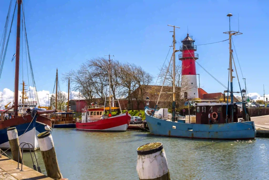 Büsum mit Hund: Perfekter Nordsee-Urlaub mit Vierbeiner 6 Hafen von Büsum mit Leuchtturm und Fischerbooten unter blauem Himmel, ideal für einen Spaziergang mit Hund entlang des Wassers in Büsum.