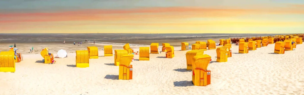 Cuxhaven mit Hund entdecken - Ferienideen für Hundebesitzer 2 Panoramaaufnahme eines breiten Sandstrandes in Cuxhaven mit zahlreichen gelben Strandkörben und Blick auf das Wattenmeer, ideal für entspannte Tage mit Hund.