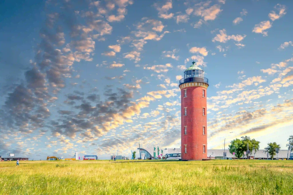 Cuxhaven mit Hund entdecken - Ferienideen für Hundebesitzer 10 Roter Leuchtturm in Cuxhaven vor einem Himmel mit dramatischen Wolken, umgeben von grünen Wiesen – ein schönes Ausflugsziel für einen Spaziergang mit Hund in Cuxhaven.