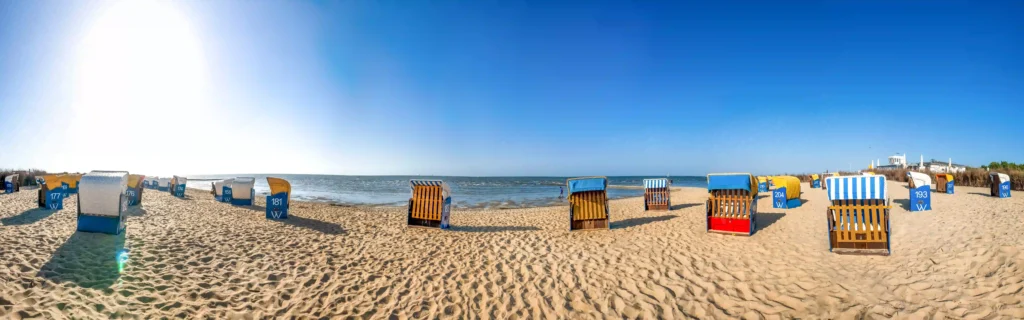Cuxhaven mit Hund entdecken - Ferienideen für Hundebesitzer 4 Zahlreiche bunte Strandkörbe am weitläufigen Sandstrand von Cuxhaven unter blauem Himmel, perfekt für einen entspannten Tag mit Hund am Meer.