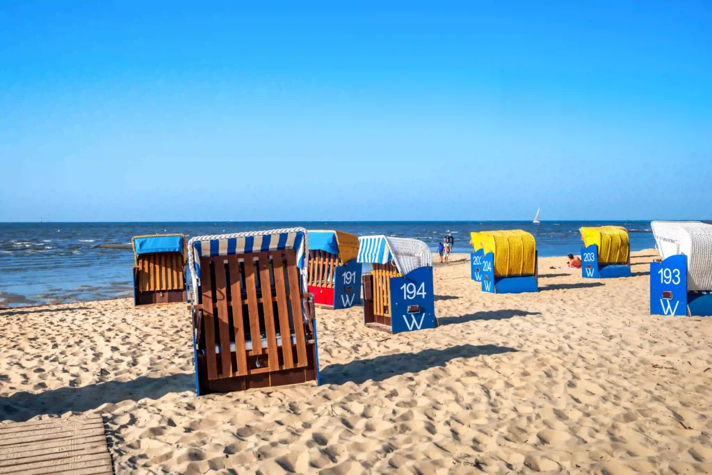 Cuxhaven mit Hund entdecken - Ferienideen für Hundebesitzer 3 Strandkörbe in verschiedenen Farben am Sandstrand von Cuxhaven mit Blick auf das Meer, ein beliebter Ort für Urlauber mit Hund.