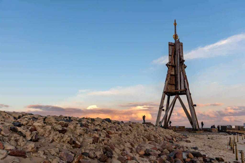 Cuxhaven mit Hund entdecken - Ferienideen für Hundebesitzer 11 Das hölzerne Wahrzeichen Kugelbake in Cuxhaven bei Sonnenuntergang, umgeben von Steinen und Sand, ein beliebtes Fotomotiv bei einem Besuch in Cuxhaven mit Hund.