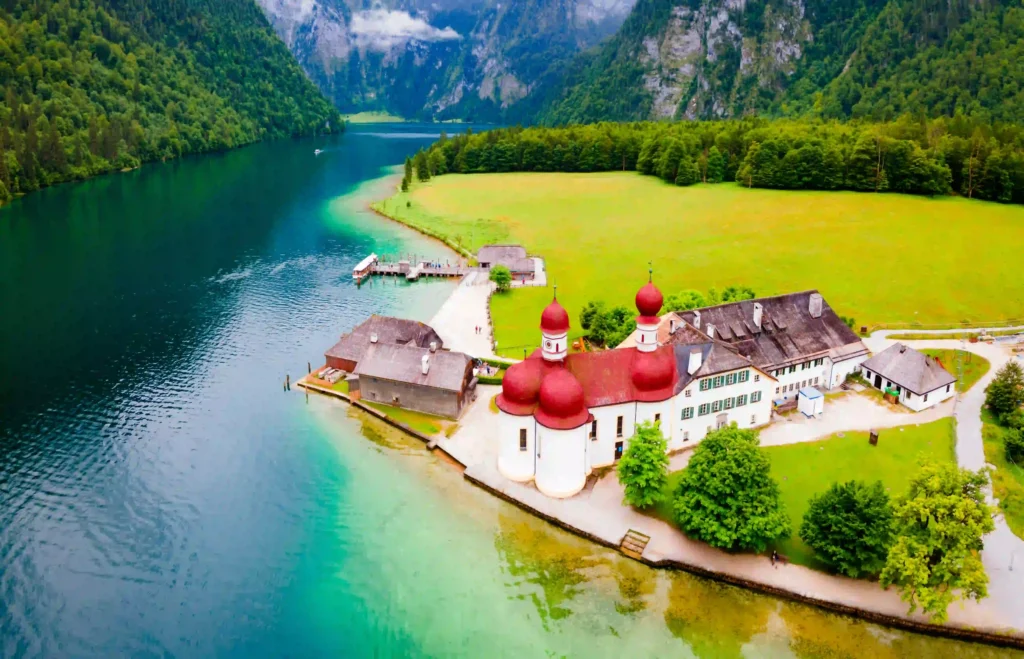 Urlaub am Königssee mit Hund: Tipps & Highlights 4 Luftaufnahme vom Königssee mit Hund, zeigt St. Bartholomä, grüne Berge, Bootsanleger und klare smaragdgrüne Seenlandschaft.