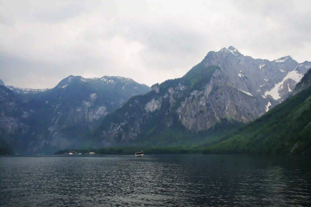 Urlaub am Königssee mit Hund: Tipps & Highlights 6 Königssee mit Hund: ruhiger See mit Boot, umgeben von schneebedeckten Bergen und dichten Wäldern im Hintergrund.