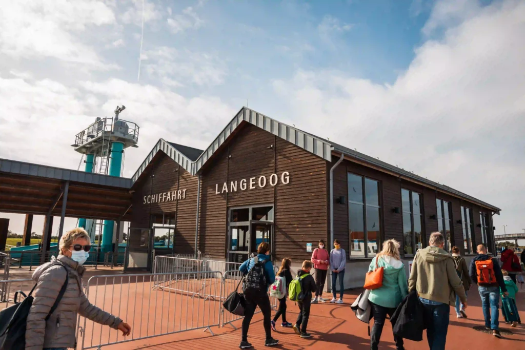 Langeoog mit Hund: dein Perfekter Inselurlaub mit Vierbeiner 7 Fähranleger und Gebäude "Schifffahrt Langeoog" mit ankommenden Passagieren, der Startpunkt für Ihren Urlaub auf Langeoog mit Hund.