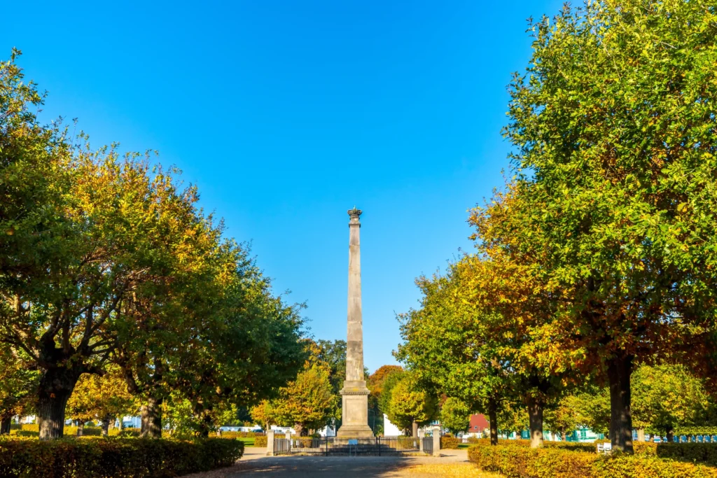 Urlaub in Putbus mit Hund – Der perfekte Guide für Rügen 6 Herbstliche Allee mit Obelisk und bunten Bäumen in Putbus, sonniger Parkweg unter klarem blauem Himmel