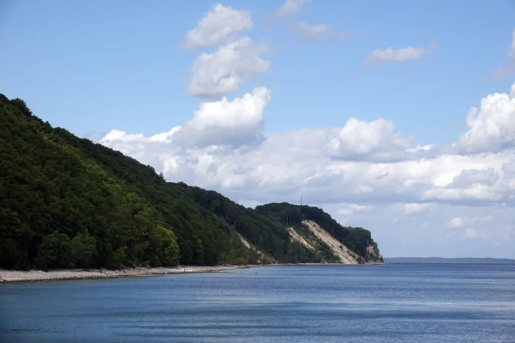 Urlaub mit Hund in Sellin auf Rügen – Dein perfekter Ostsee-Guide 9 Sellin Küstenlandschaft mit bewaldetem Steilhang, Strand, ruhigem Meer und teilweise bewölktem Himmel auf Rügen