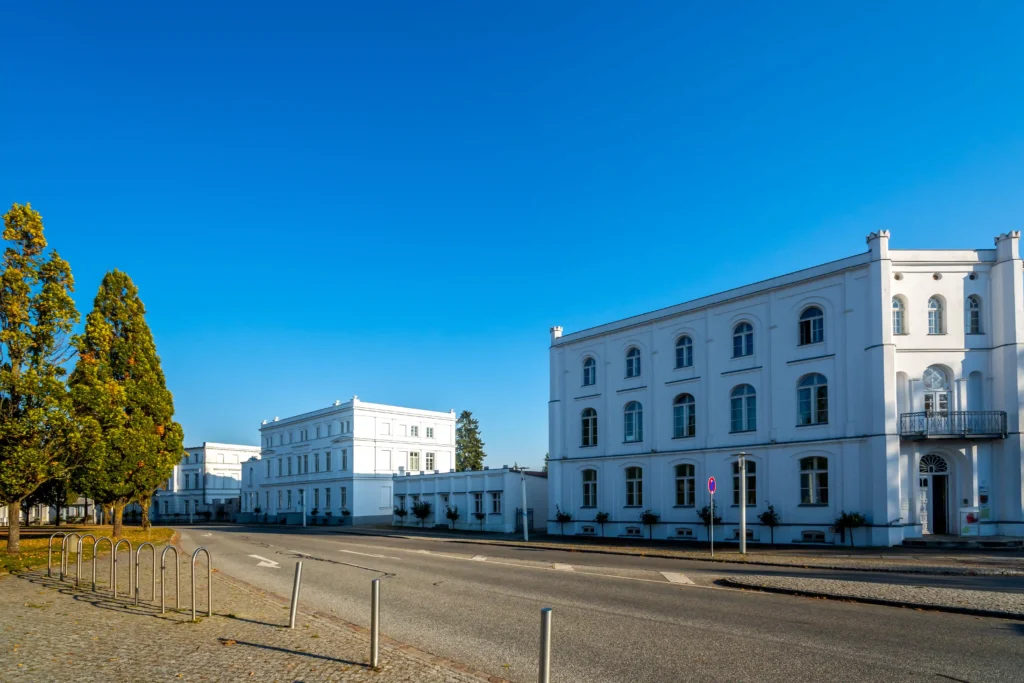 Urlaub in Putbus mit Hund – Der perfekte Guide für Rügen 5 Straße in Putbus mit weißen Gebäuden, Fahrradständern, herbstlichen Bäumen und blauem Himmel bei Tageslicht.