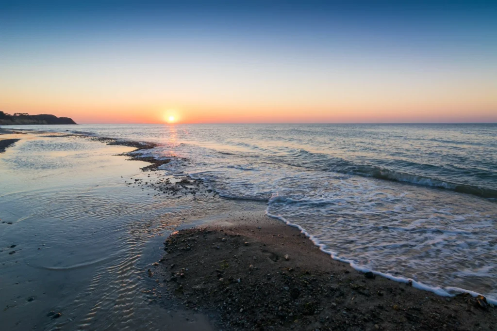 Dranske Ausflugsziele: Perfekter Urlaub mit Hund auf Rügen 3 Sonnenuntergang am ruhigen Strand von Dranske mit orangefarbenem Himmel, sanften Wellen und felsiger Küste im Hintergrund