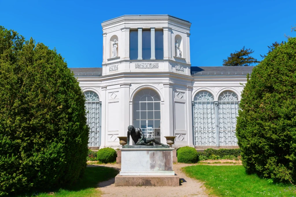 Urlaub in Putbus mit Hund – Der perfekte Guide für Rügen 2 Elegantes weißes Schloss in Putbus mit zentralem achteckigem Turm, dunkler Statue und grünem Park bei blauem Himmel