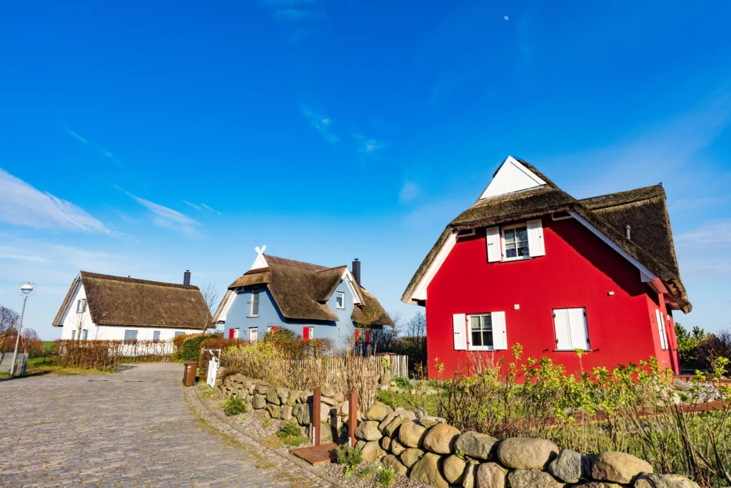 Ausflug Kap Arkona mit Hund: Dein kompletter Guide für Rügen 8 Traditionelle reetgedeckte Häuser mit roter und blauer Fassade am Kap Arkona unter klarem Himmel mit Mondsichel.