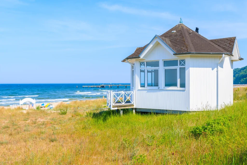 Urlaub Göhren mit Hund: Perfekte Ferien auf Rügen 3 Weißes Haus am Strand mit Pier, Meer und Vegetation in Göhren auf Rügen unter klarem blauem Himmel.