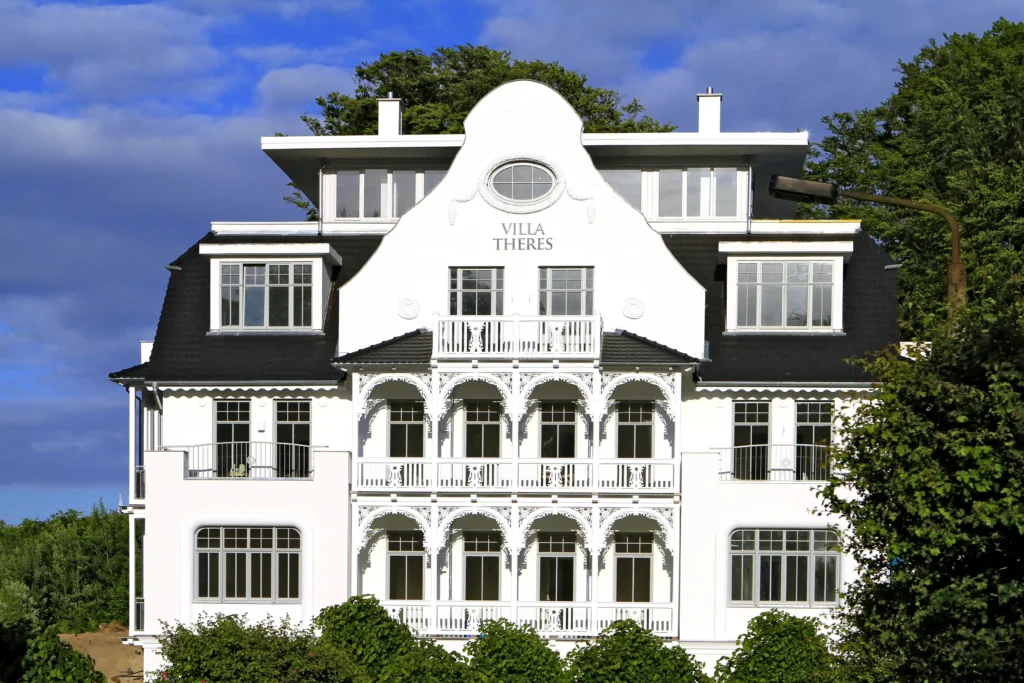 Urlaub mit Hund in Sellin auf Rügen – Dein perfekter Ostsee-Guide 6 Großes Haus umgeben von Bäumen unter blauem Himmel in Sellin auf Rügen, idyllische Landschaft und Naturkulisse.