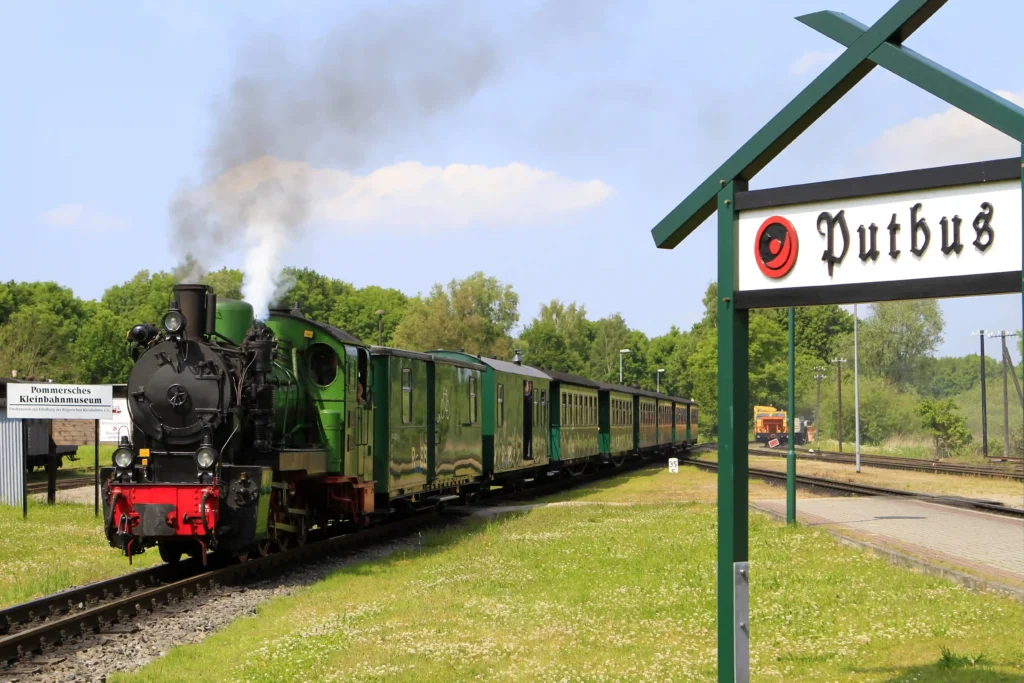 Urlaub in Putbus mit Hund – Der perfekte Guide für Rügen 8 Dampflokomotive mit grünen Wagen am Bahnhof Putbus vor grünem Wald und blauem Himmel an sonnigem Tag