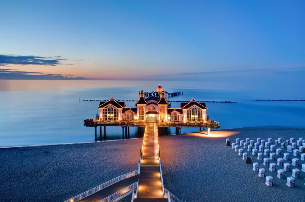 Urlaub mit Hund in Sellin auf Rügen – Dein perfekter Ostsee-Guide 10 Sellin auf Rügen: Lange Seebrücke mit weißem Gebäude bei Sonnenaufgang, ruhiges Wasser und dramatischer Himmel am Strand.