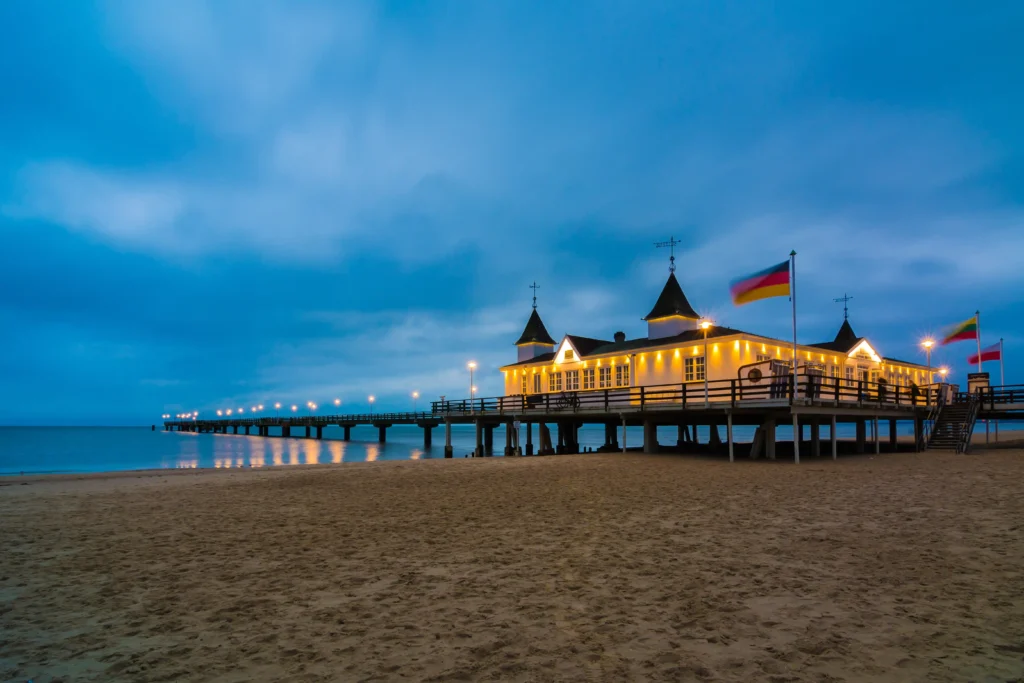 Ferien mit Hund im Seebad Ahlbeck – Entspannung pur 26 Beleuchteter Pier bei Dämmerung mit Strand und Gebäude, ideal für Ferien mit Hund in Ahlbeck am Meer.