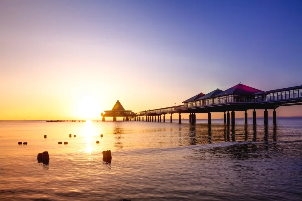 Urlaub mit Hund in Heringsdorf: Dein perfekter Ostsee-Guide 22 Sonnenaufgang über der Seebrücke in Heringsdorf mit Hund, ruhiges Meer und bunte Himmelstöne am Wasserufer.