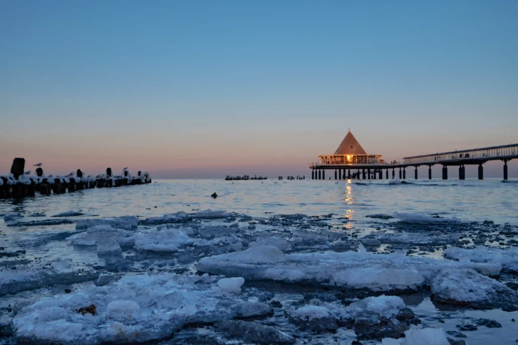 Urlaub mit Hund in Heringsdorf: Dein perfekter Ostsee-Guide 25 Heringsdorf mit Hund: Pier bei Dämmerung mit Eisflächen, beleuchtetem Gebäude und Spaziergängern am Wasserufer
