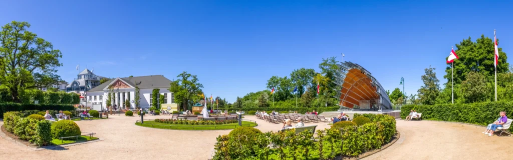 Urlaub mit Hund in Heringsdorf: Dein perfekter Ostsee-Guide 23 Sonniger Park in Heringsdorf mit Hund, mit Brunnen, Bänken, Flaggen und Spaziergängern auf gepflegten Wegen und Grünflächen.
