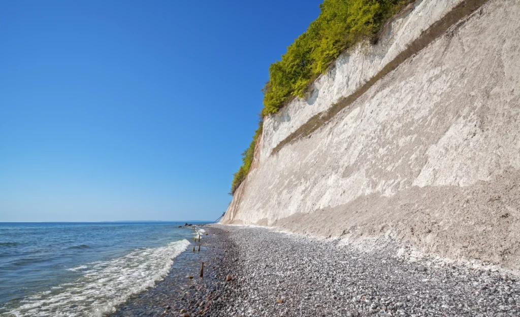 Wanderung Königsstuhl mit Hund: Perfekter Guide für Kreidefelsen 8 Wanderung Königsstuhl: Küstenlandschaft mit blauem Himmel, ruhigem Meer, Kiesstrand, Holzpfählen und weißem Kreidefelsen