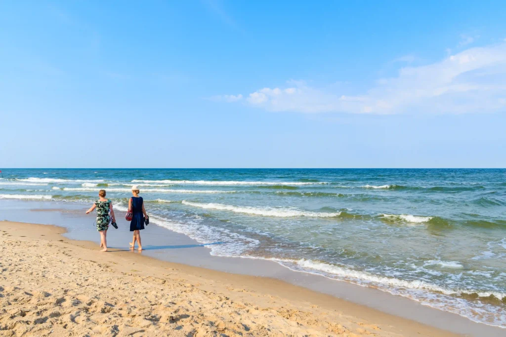 Urlaub mit Hund in Baabe auf Rügen: Top Tipps & Guide 3 Zwei Frauen am Strand von Baabe Rügen gehen barfuß am Wasser entlang bei sonnigem Himmel und ruhiger Ostsee.