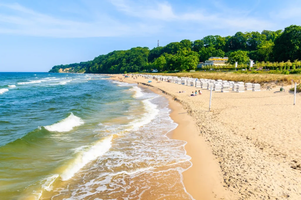 Urlaub mit Hund in Baabe auf Rügen: Top Tipps & Guide 2 Strand von Baabe Rügen mit türkisfarbenem Meer, weißen Strandkörben, Volleyballnetz und grünem bewaldetem Hügel im Hintergrund