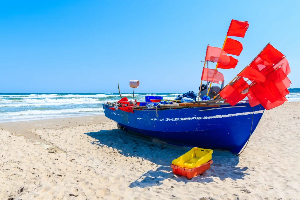 Urlaub mit Hund in Baabe auf Rügen: Top Tipps & Guide 8 Blaues Fischerboot mit roten Flaggen am Sandstrand von Baabe Rügen, klarer Himmel und ruhiges Meer im Hintergrund