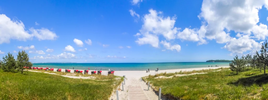 Dein perfekter Ausflug zum Hundestrand Binz 3 Panoramablick auf den sonnigen Strand von Binz mit blauem Himmel, Dünen, Strandkörben und klarem Meerwasser.