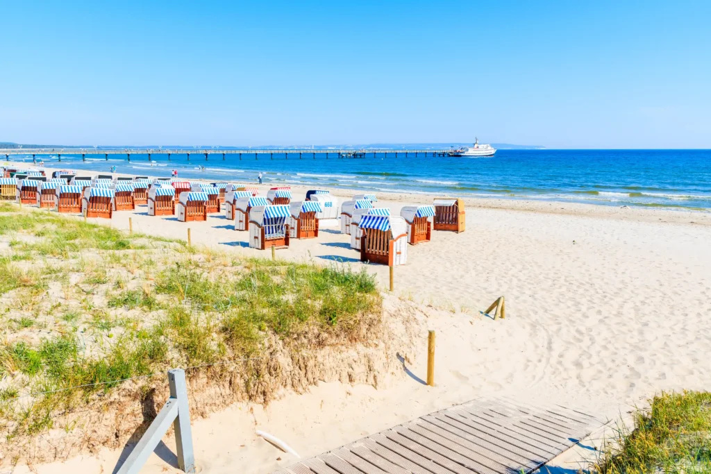 Dein perfekter Ausflug zum Hundestrand Binz 6 Strand mit Strandkörben, Pier, Boot und Dünen an einem sonnigen Tag in Binz an der Ostsee.